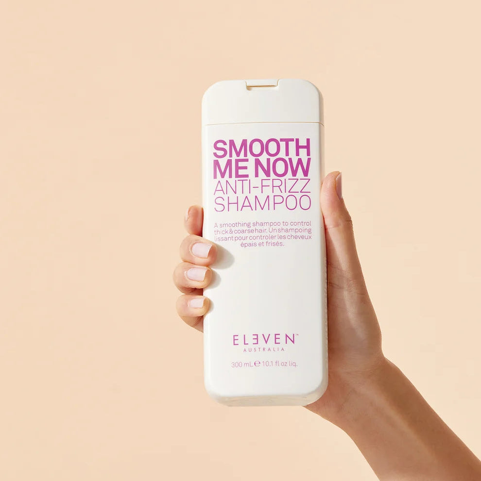 Hand holding a bottle of 'Smooth Me Now Anti-Frizz Shampoo' by Elvien against a beige background