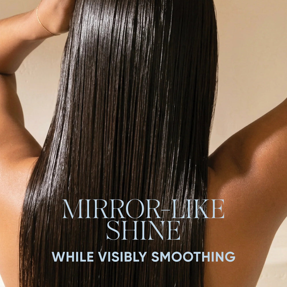 A person shown from the back with long, straight, glossy dark hair and arms raised, holding a comb near the scalp. Text at the top reads 'SIGNATURE SENSES POWERED BY BIOTECH ACTIVES' and the lower text reads 'MIRROR-LIKE SHINE WHILE VISIBLY SMOOTHING.