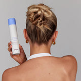 Woman with beautiful upstyle hair holding a bottle of Juuce Stuck Up Lacquer with a gray background