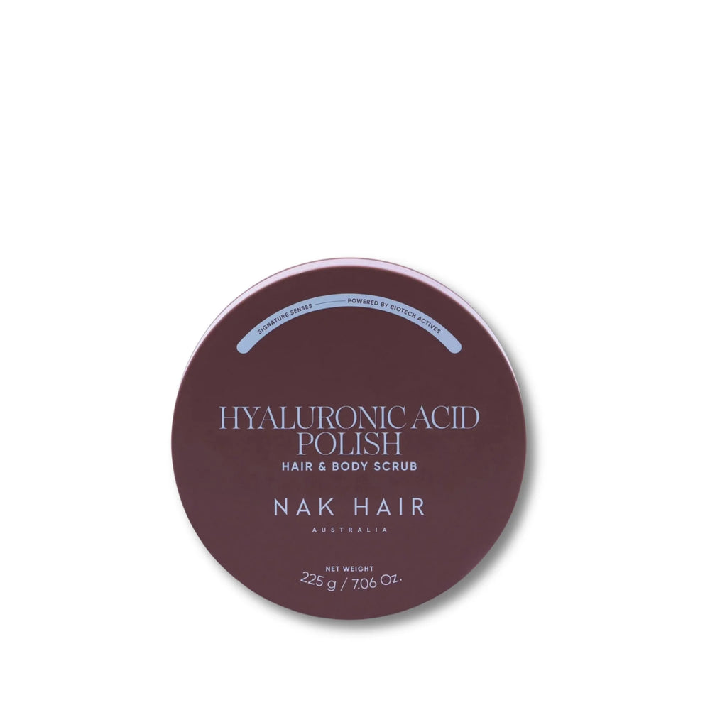 A round dark mauve-brown tin of NAK HAIR Hyaluronic Acid Polish Hair & Body Scrub on a clean white background.