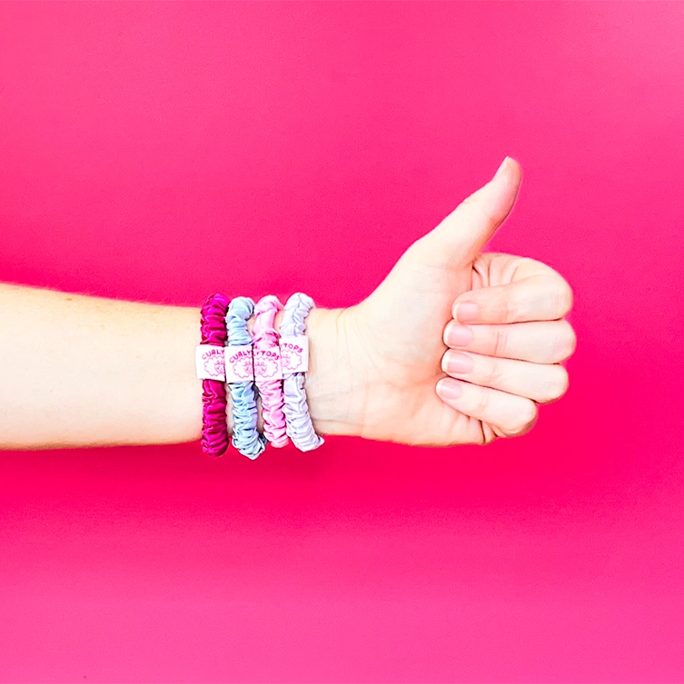 Hand giving a thumbs up with colorful hair ties on a pink background